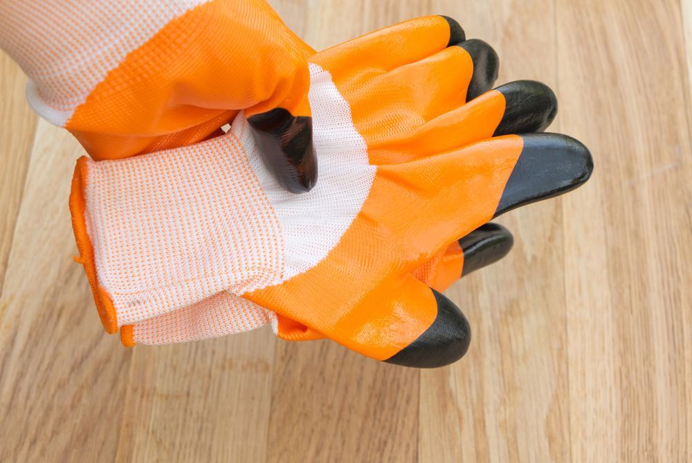 Guanti da lavoro arancioni e neri tenuti sopra una superficie di legno