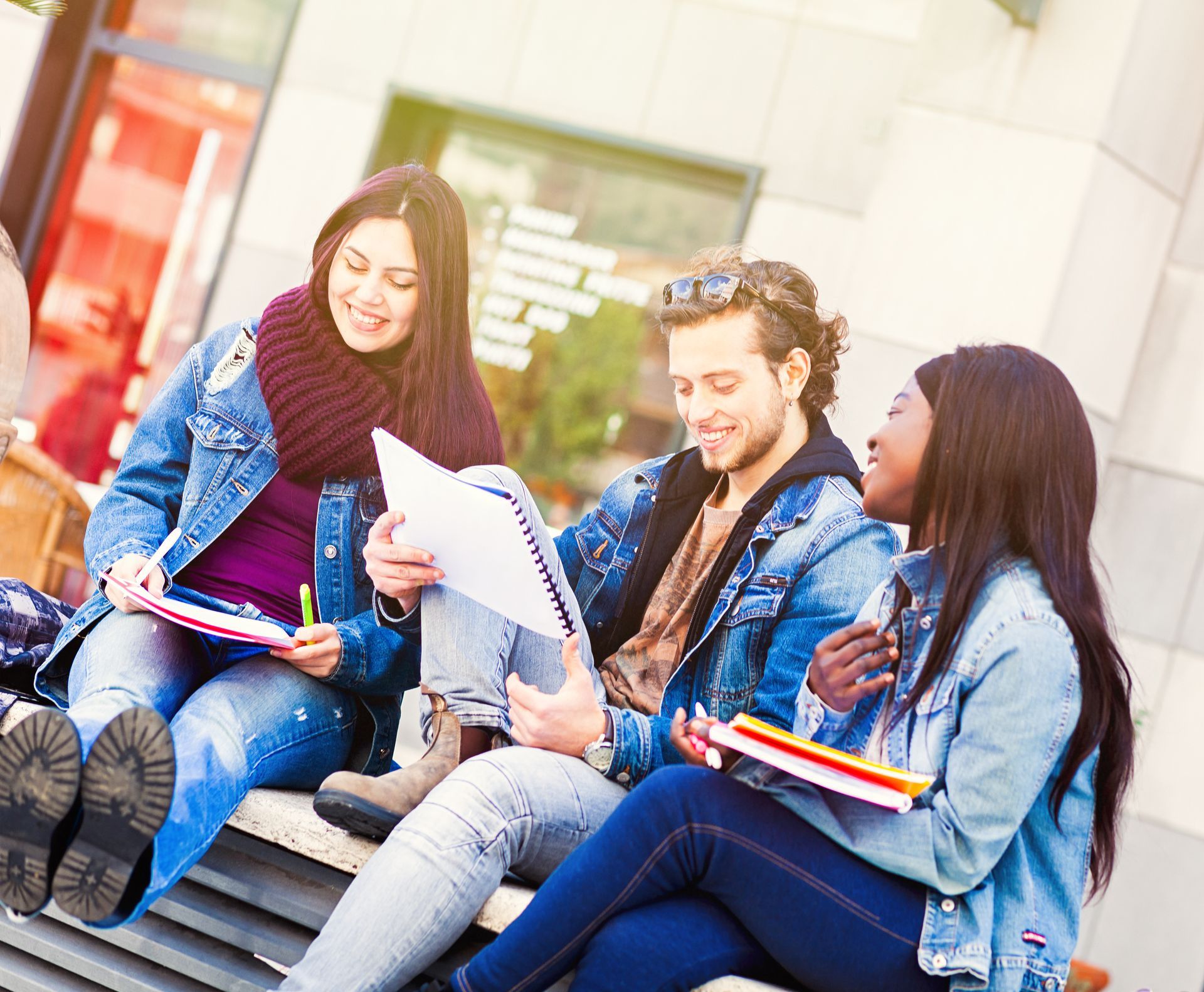 Des étudiants assis dehors, cahiers à la main, sur un banc ensoleillé du campus