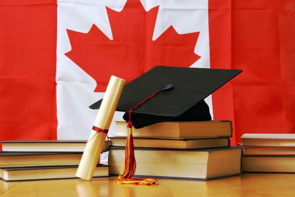 Toque et diplôme de remise de diplôme sur une pile de livres, avec le drapeau canadien en arrière-plan.
