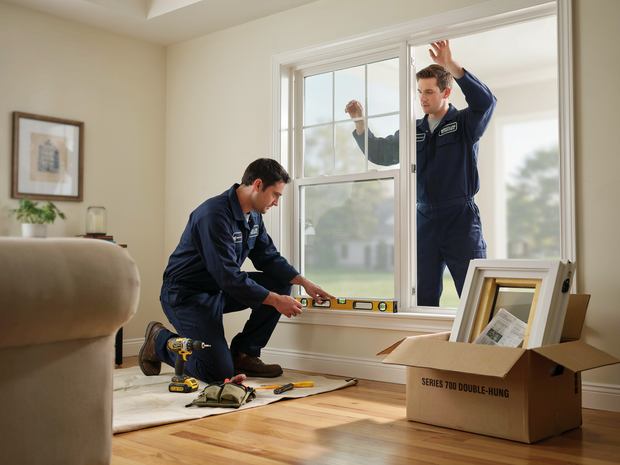 Two movers unpacking boxes in a bright living room beside a large window