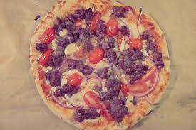 A pizza with meat , tomatoes , onions and cheese on a table.