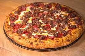 A pizza with a lot of toppings on it is sitting on a wooden table.