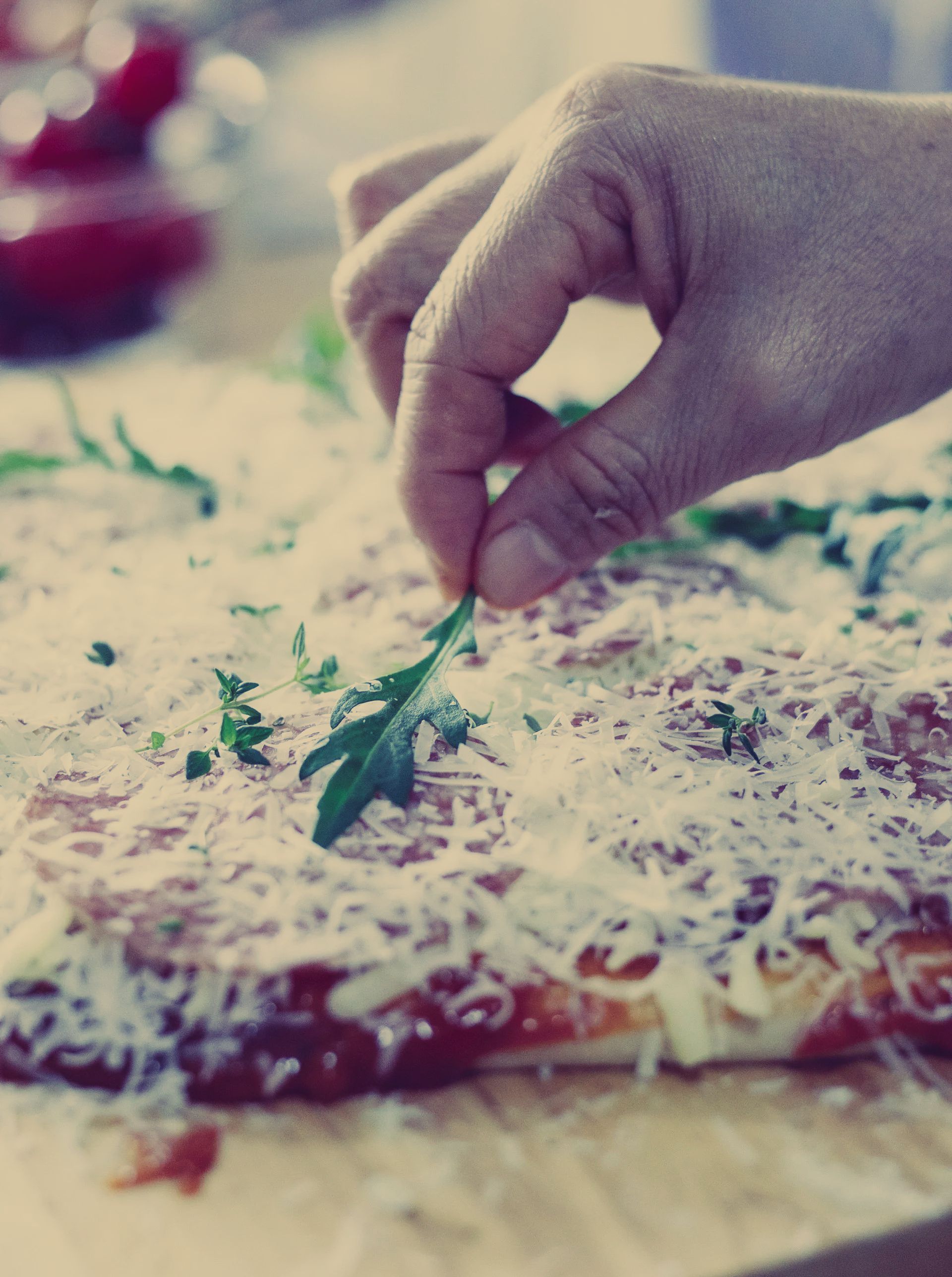 A person is putting a green leaf on top of a pizza