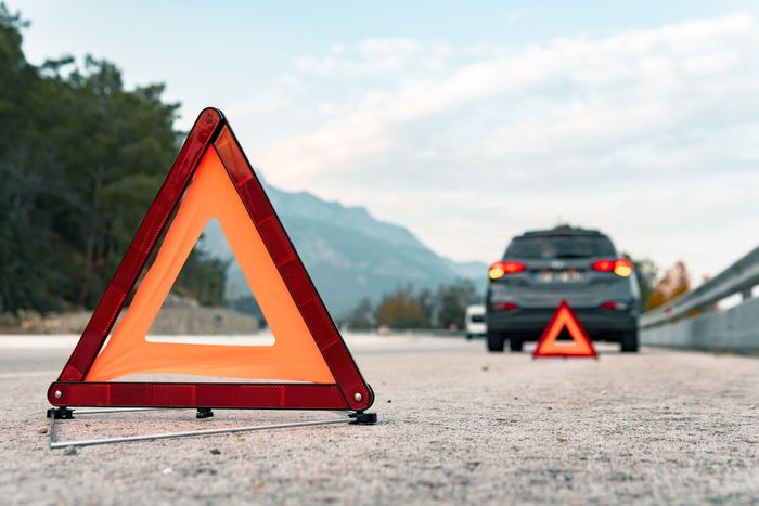 A car is sitting on the side of the road next to a warning triangle.