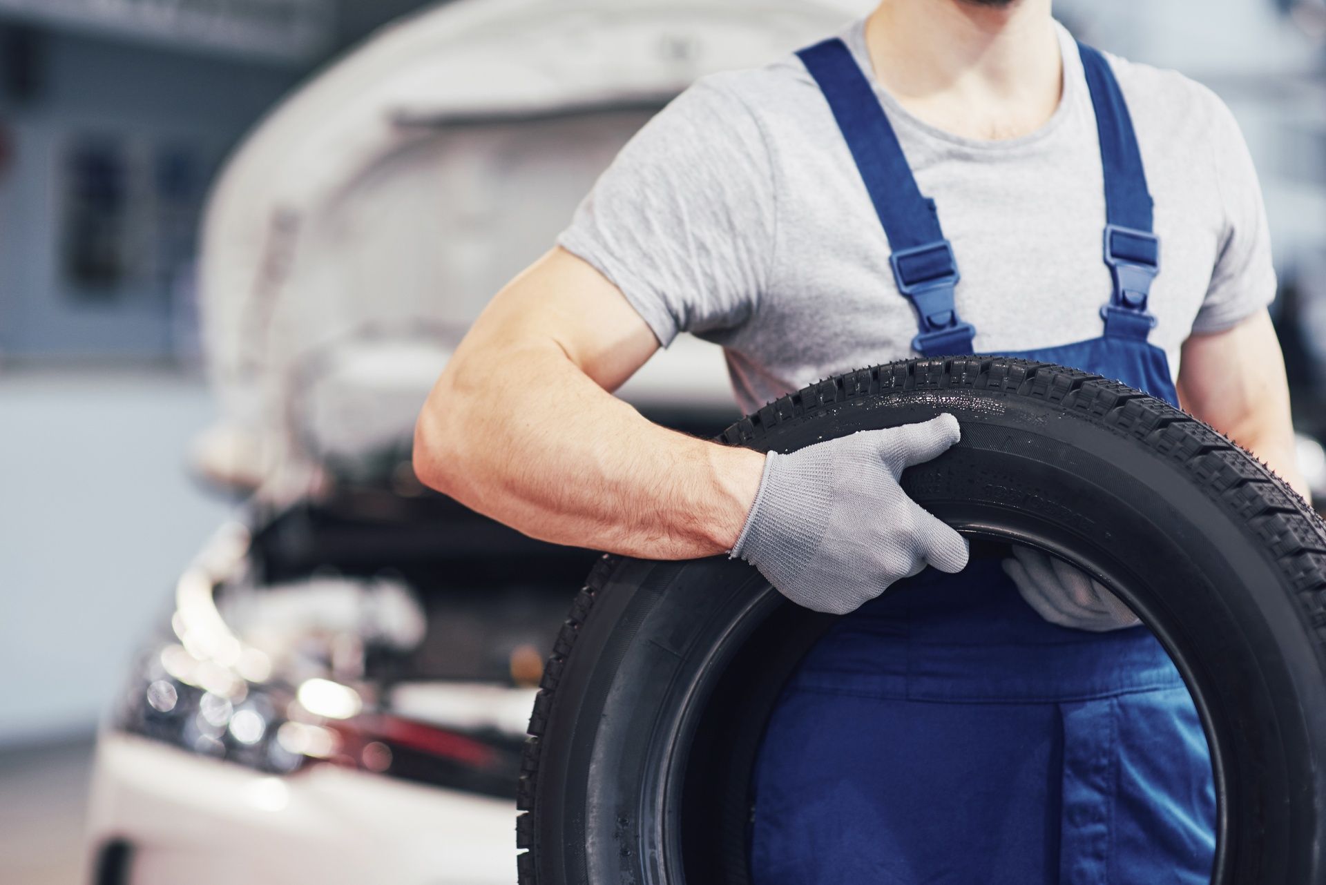A man is holding a tire in front of a car.