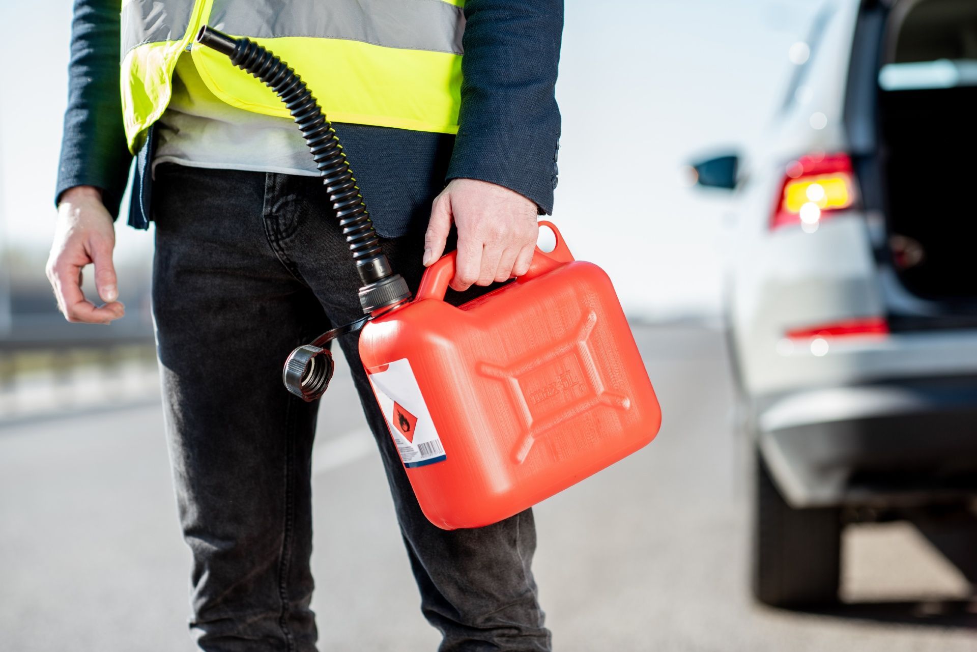 A man is holding a gas can next to a car on the side of the road.