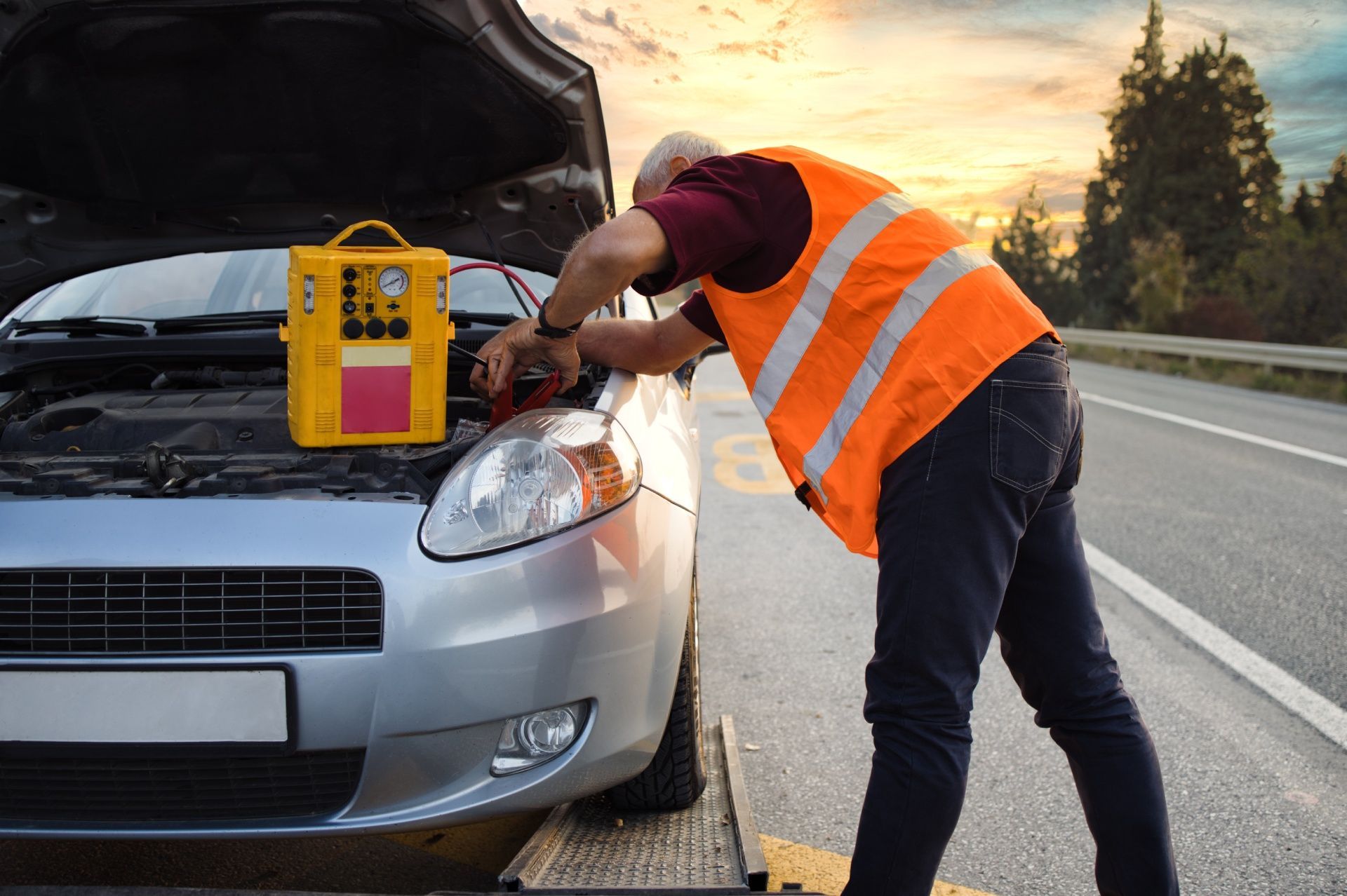 A man is working on a broken down car on the side of the road.