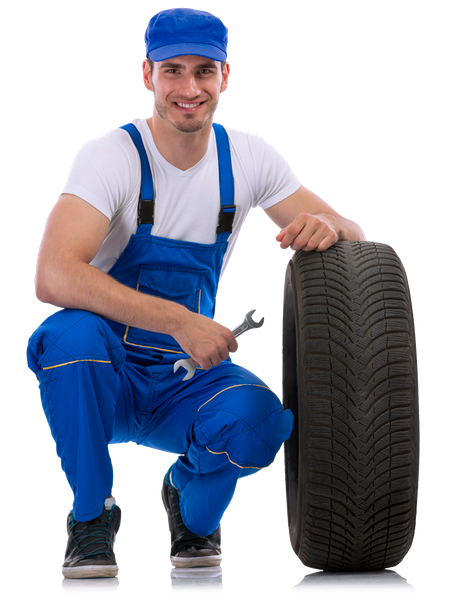 A man in blue overalls is kneeling next to a tire and holding a wrench.