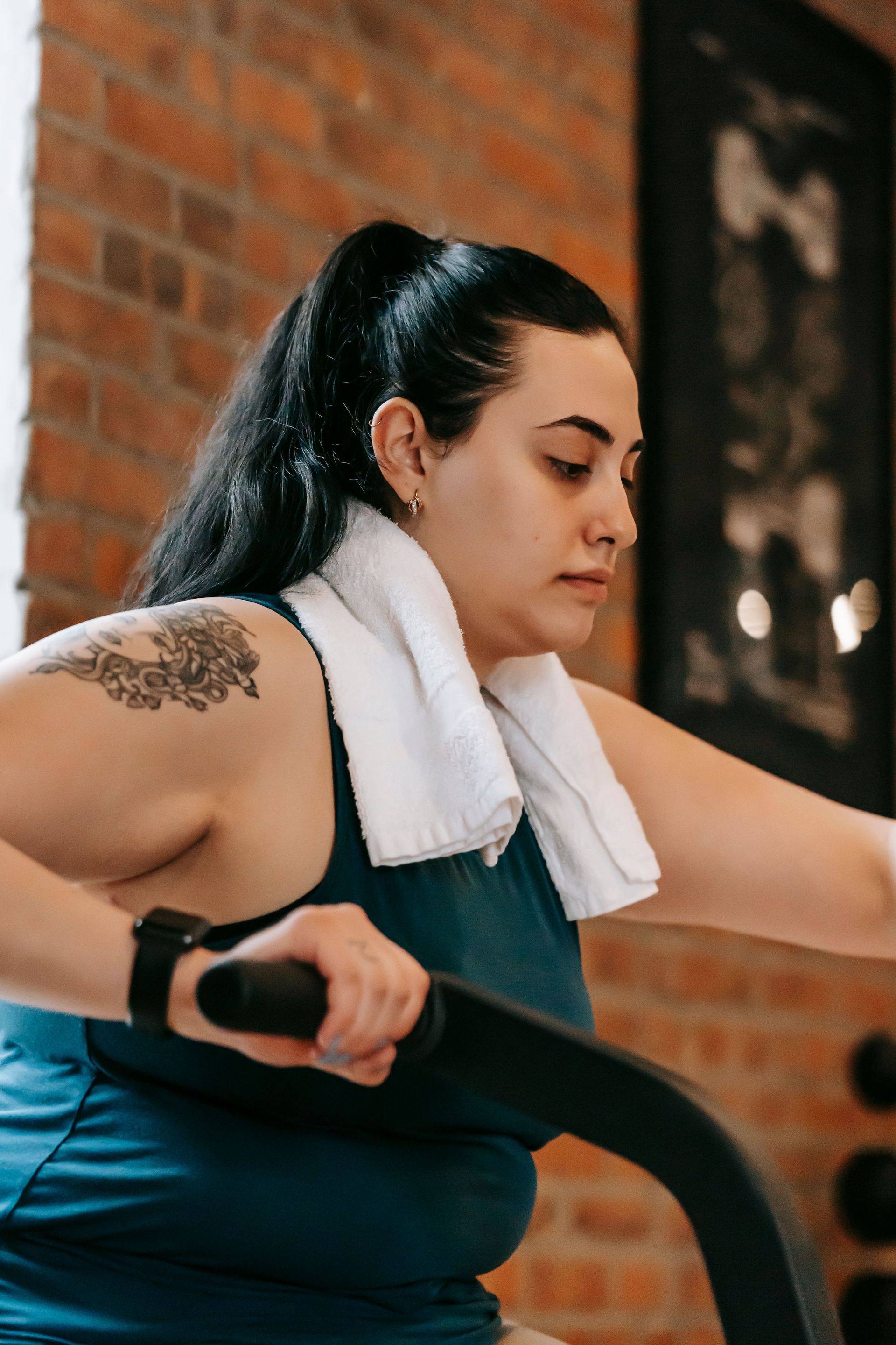 Person using a stair climber with a white towel around the neck in a brick-walled gym