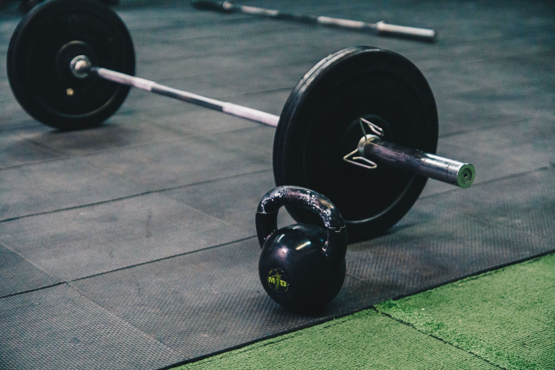 Barbell with black plates and a kettlebell on a gym floor mat