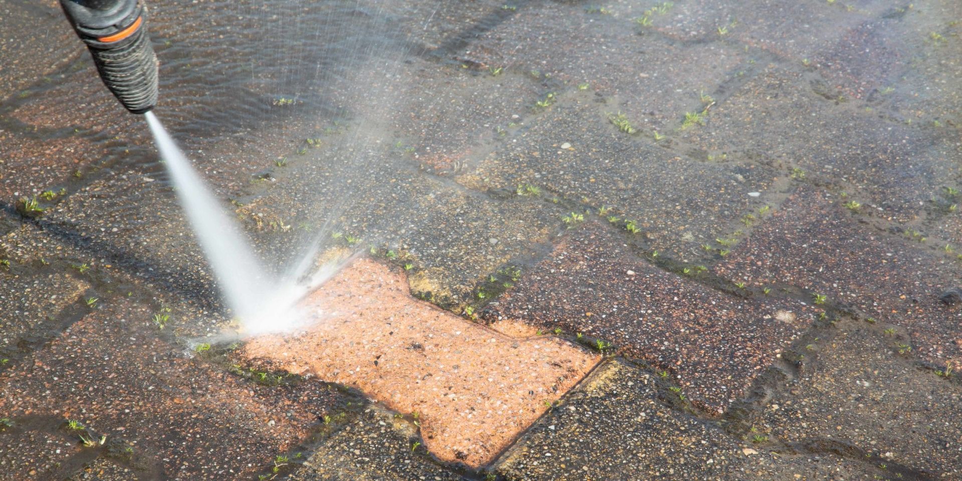 Pressure washing a brick patio, with a bright spray cleaning a small section.
