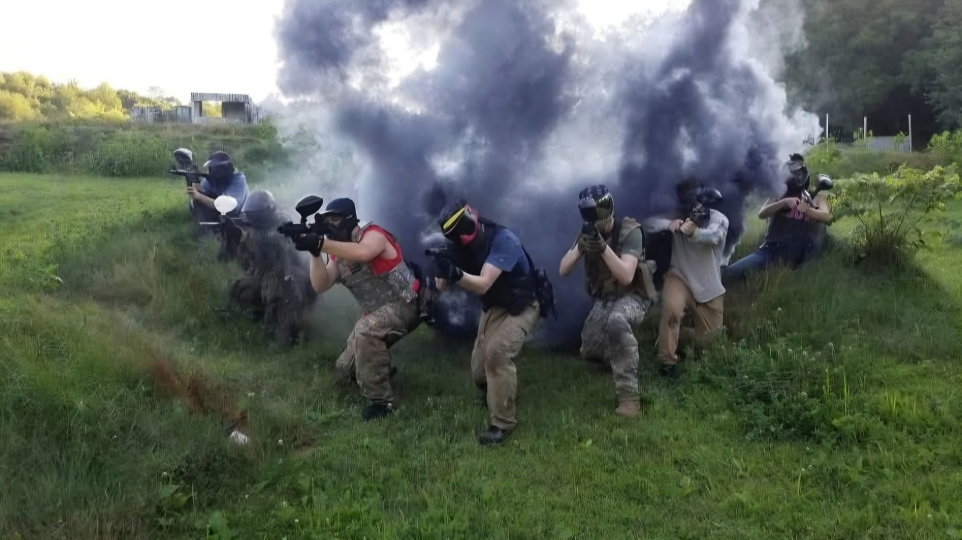 People in tactical gear crouch and move through grassy terrain as thick smoke billows behind them.