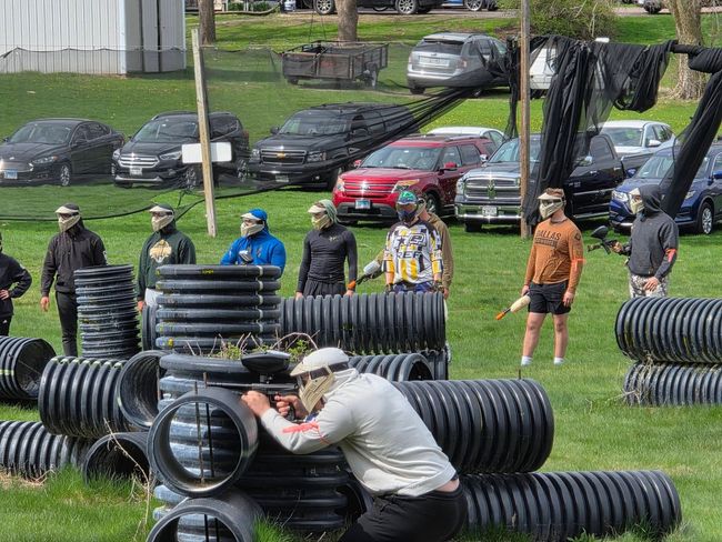 People standing by large black pipes on a grassy field, with one person leaning over a pipe in front.