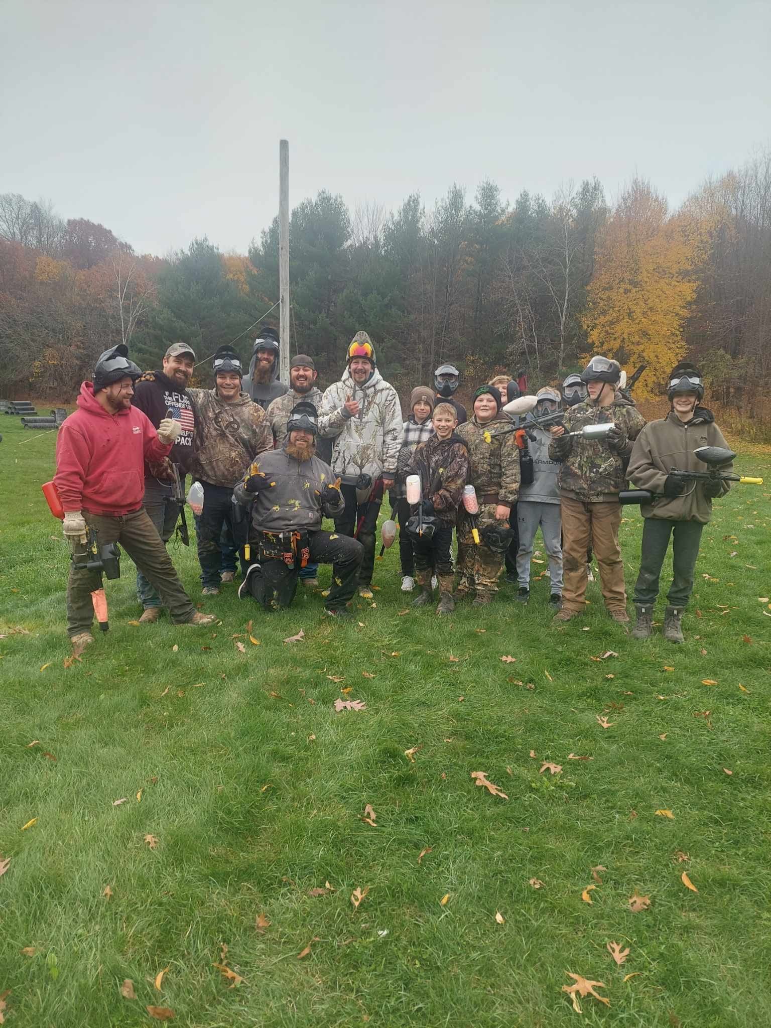 Group of people posing outdoors on a grassy field with autumn trees in the background, some wearing colorful jackets.