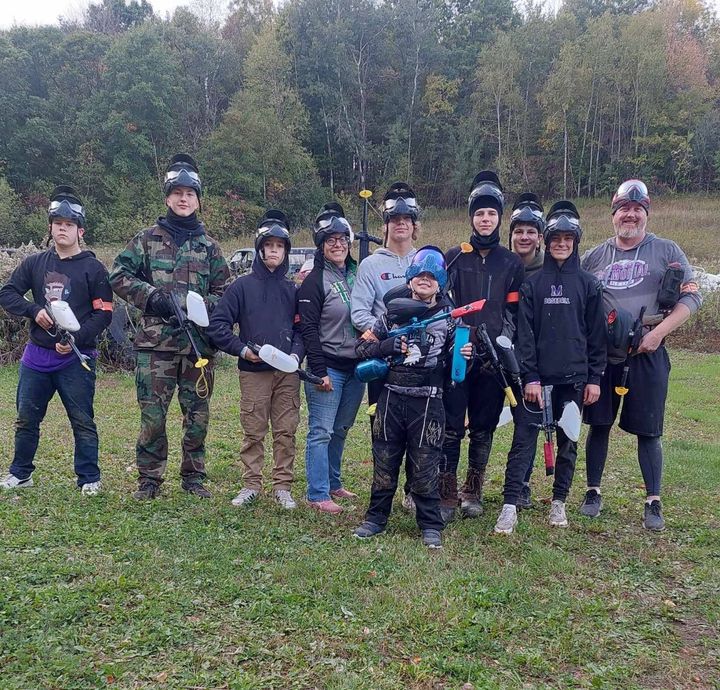 Paintball team posing outdoors on a grassy field, holding markers and wearing protective gear