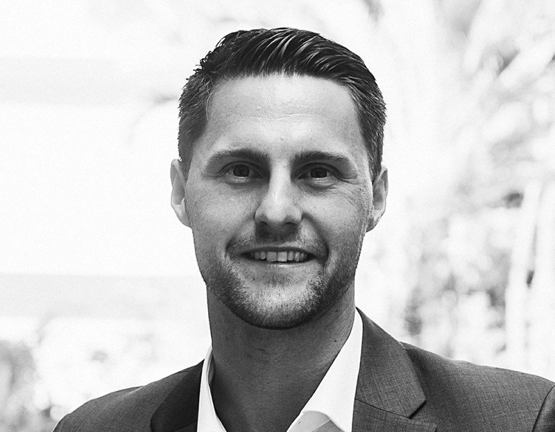 A man in a suit and tie is smiling in a black and white photo.