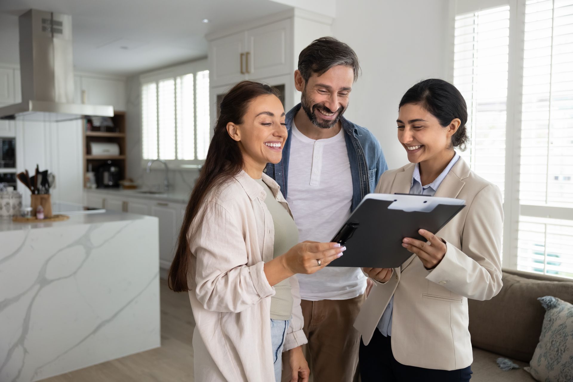 A smiling couple reviewing renters insurance paperwork with an agent in a bright, modern kitchen