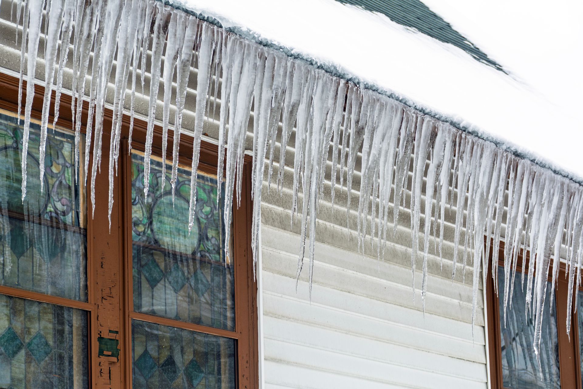 Large icicles hanging from a snow covered roof edge above exterior windows.