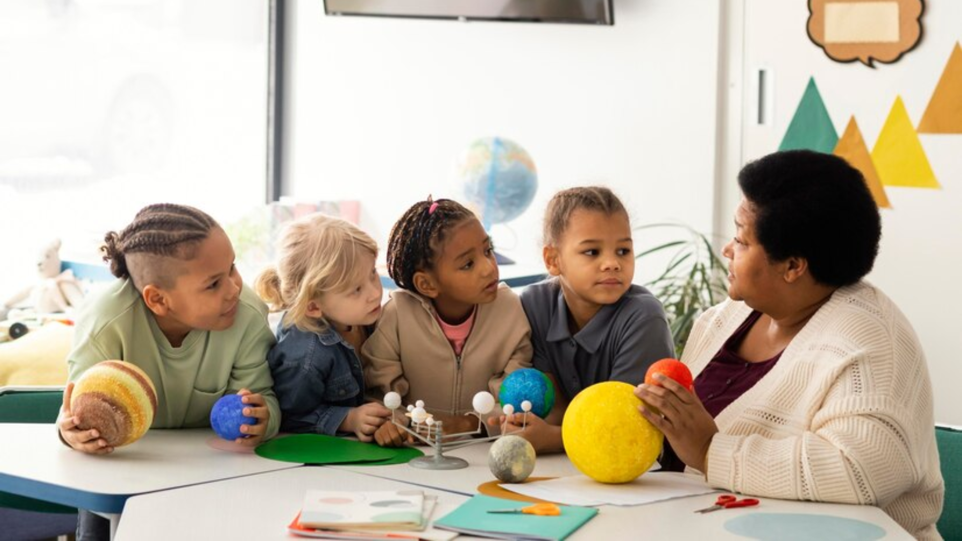 Teacher showing solar system models to group of students in a classroom.