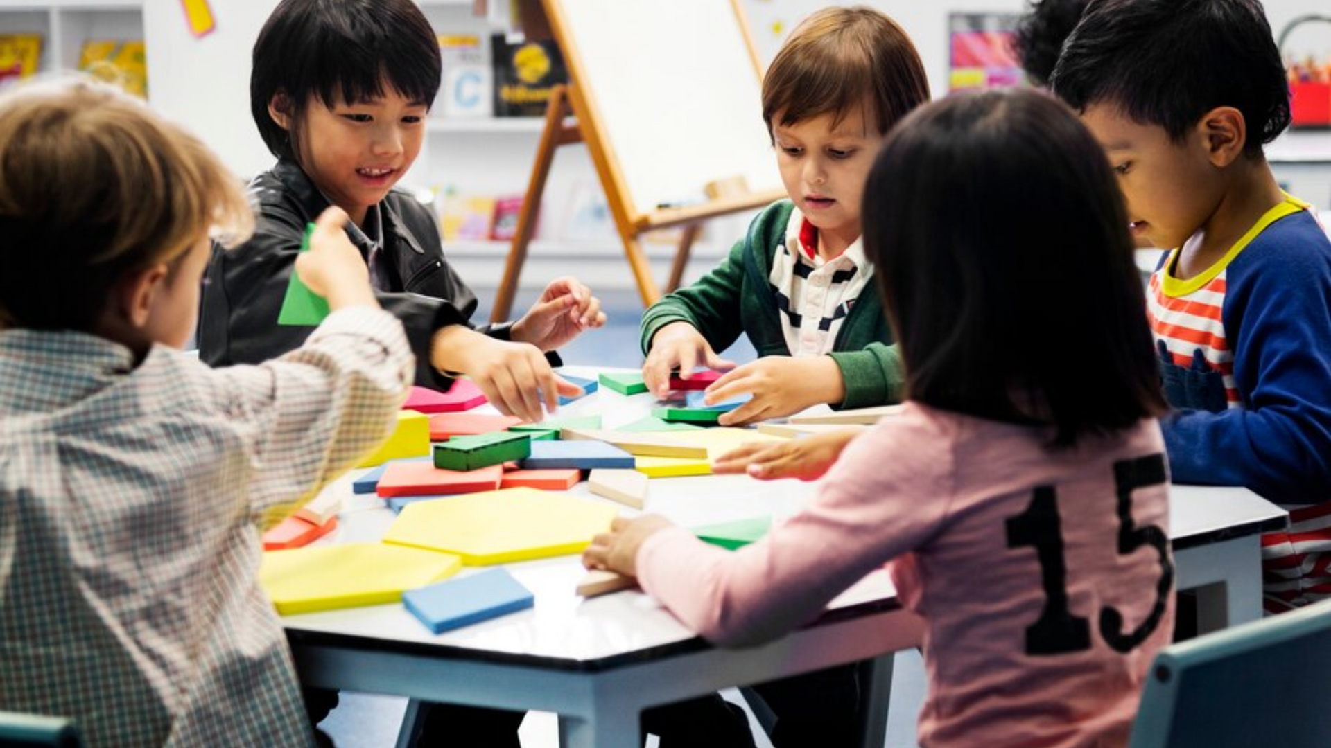 Children seated at a table in a classroom playing with colorful blocks.
