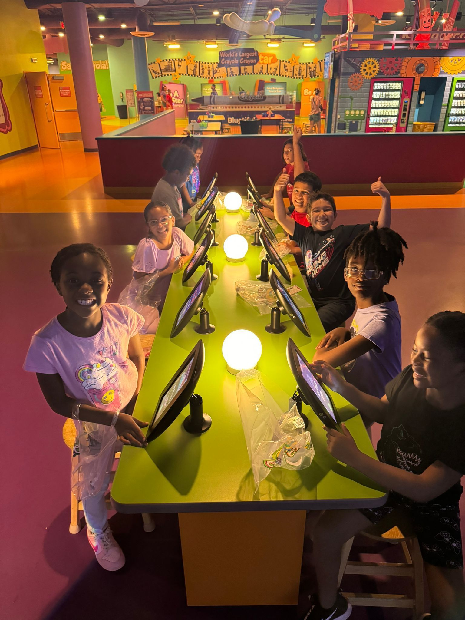 A group of children are sitting at a long table with computers.