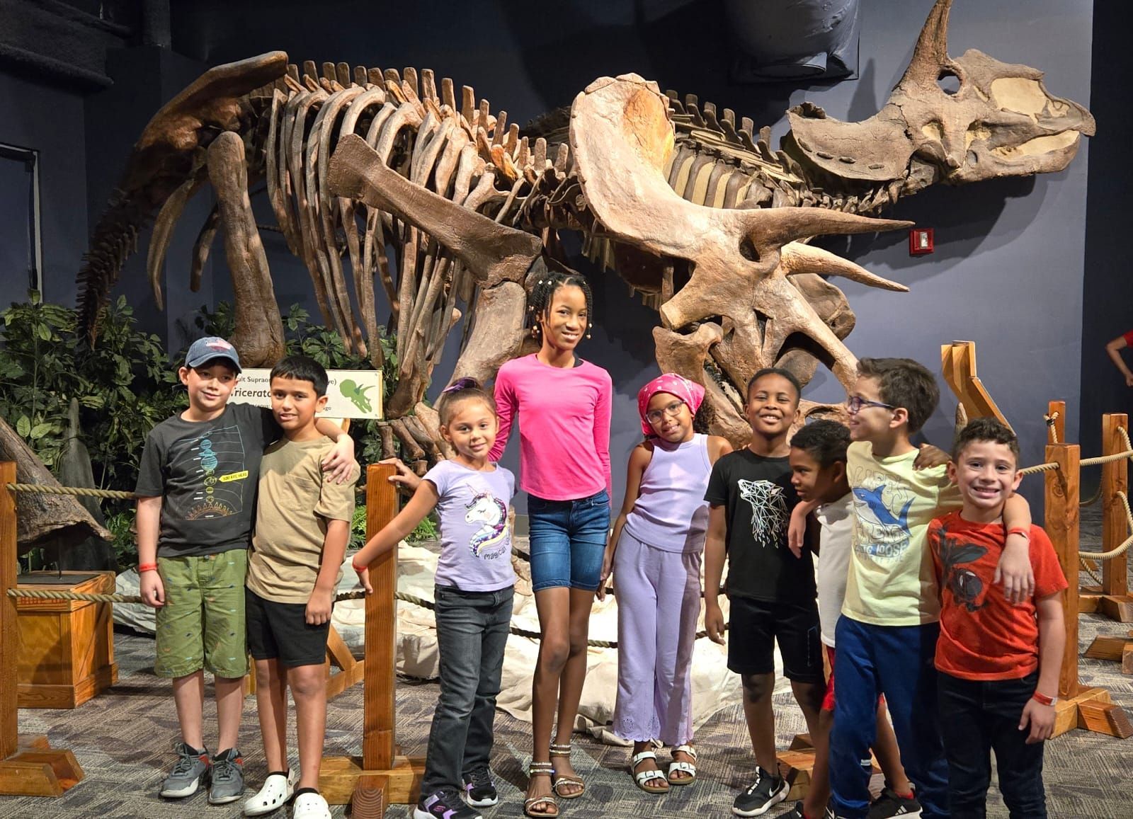 A group of children are posing for a picture in front of a dinosaur skeleton.