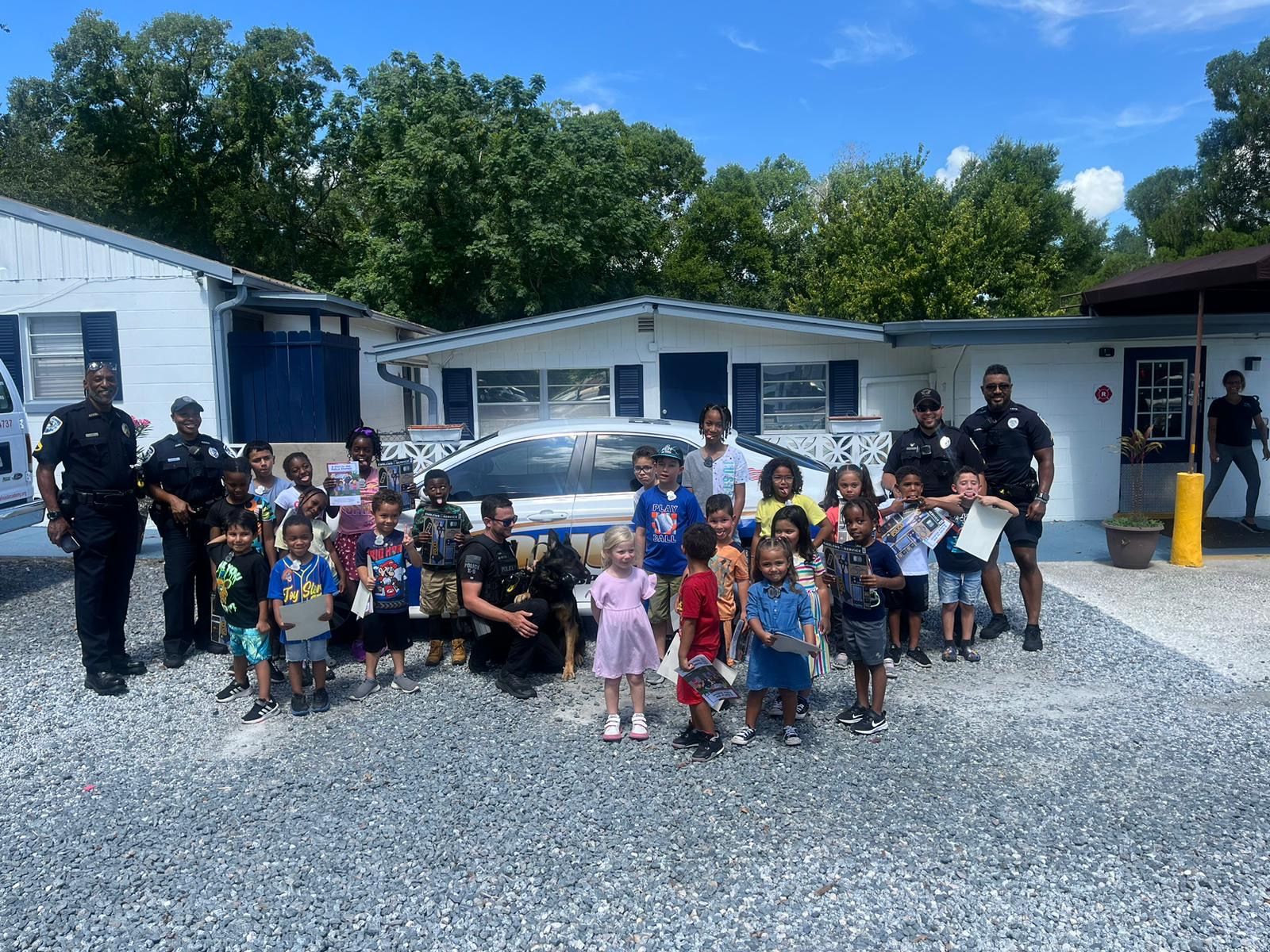 A group of children and police officers are posing for a picture in front of a house.