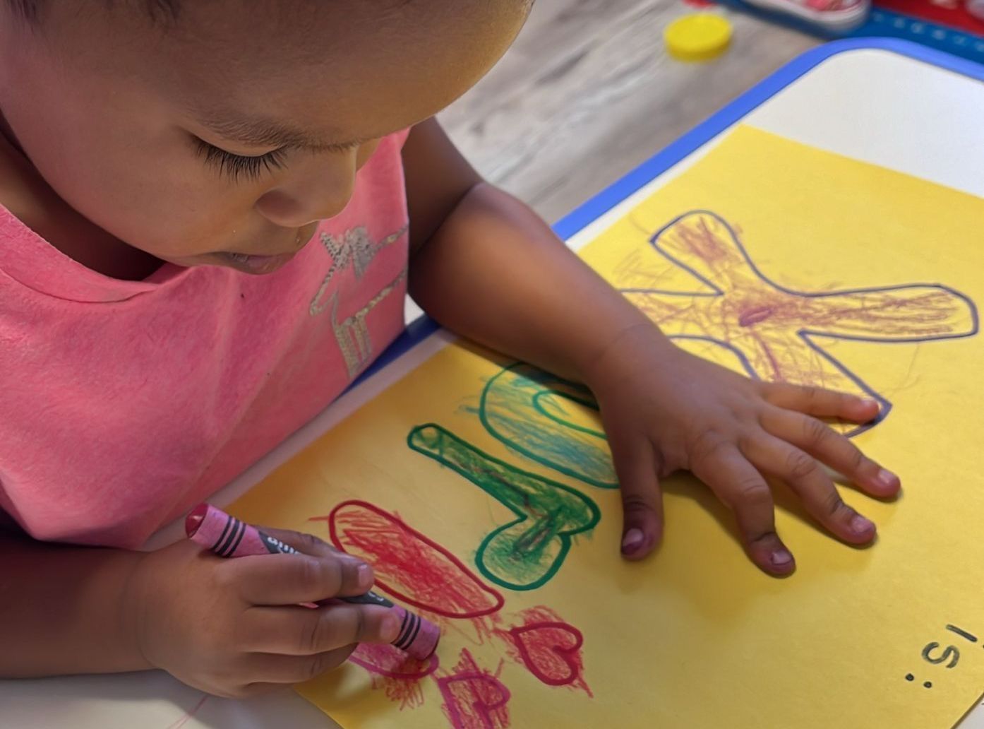 A young child coloring on yellow paper with crayons.