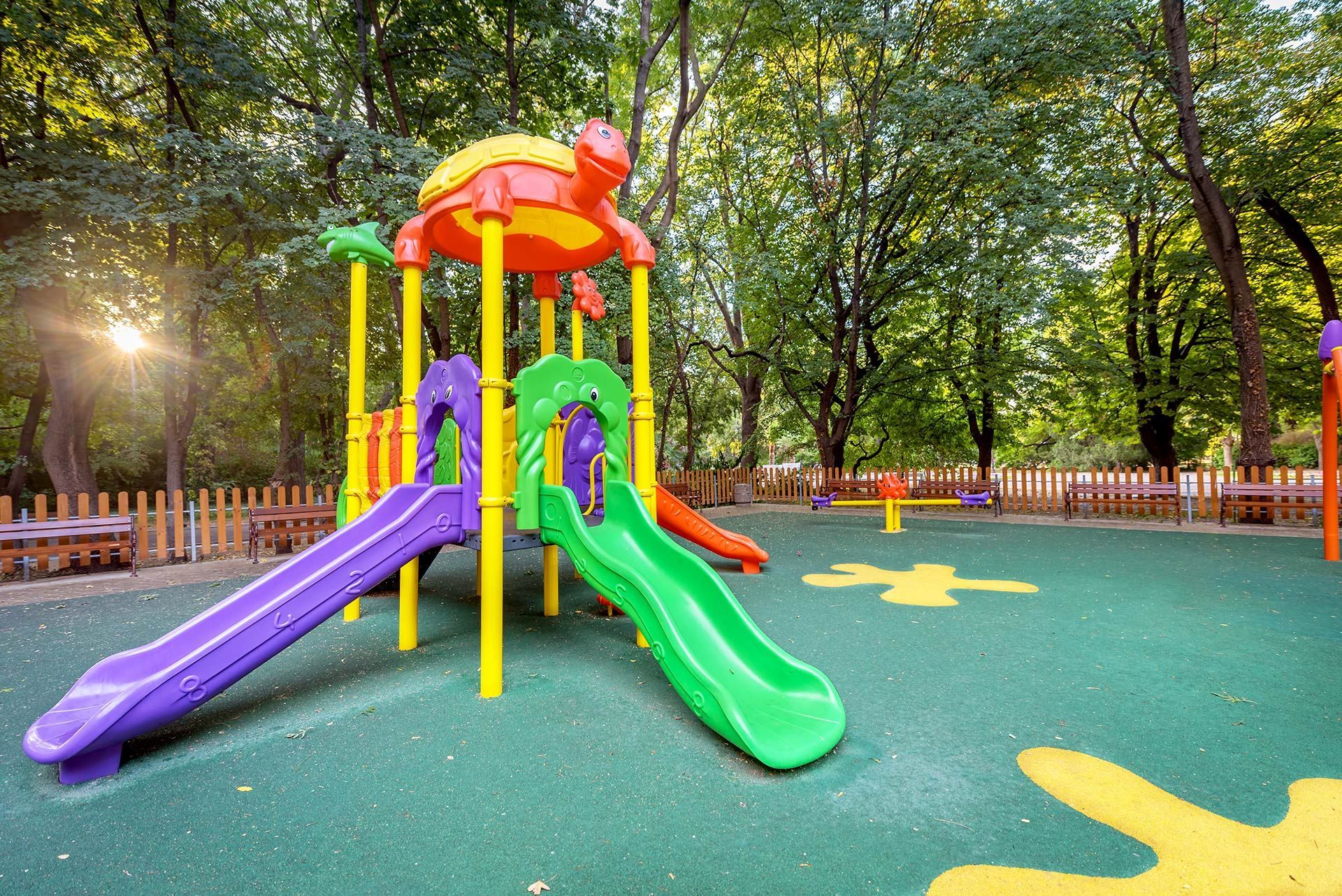 Two children sliding down a yellow slide on a playground; green turf, blue sky.