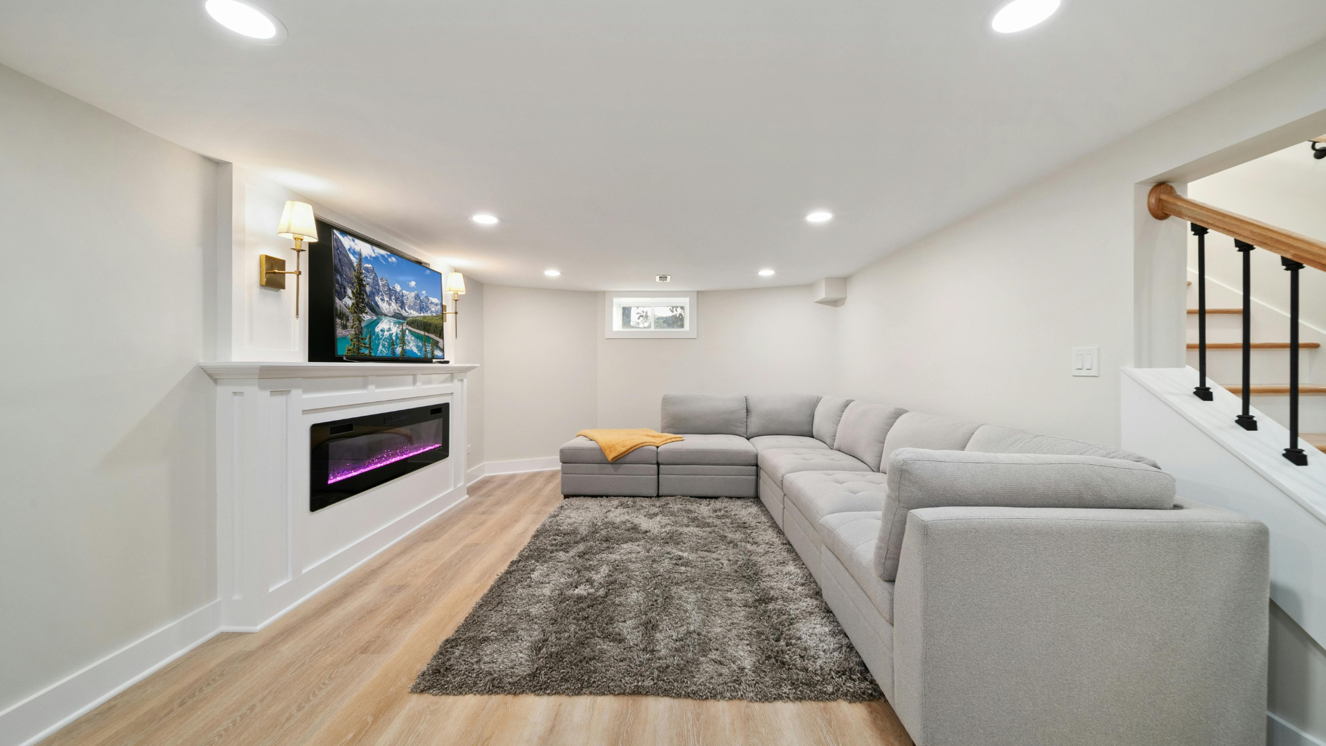 Basement living area with gray sectional, fireplace, TV, and stairs.