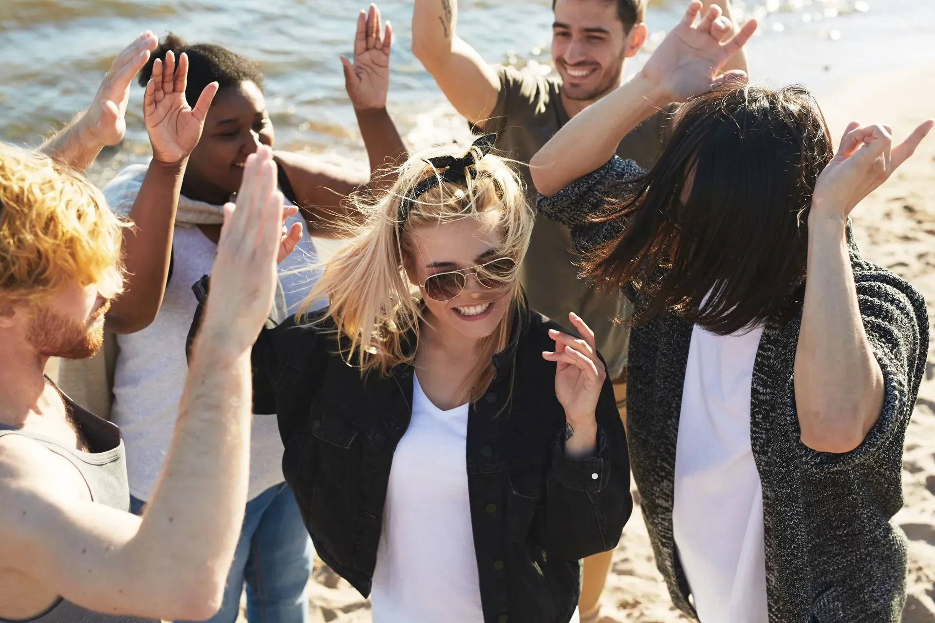 A group of people dancing and cheering with their hands raised on a sunny beach.