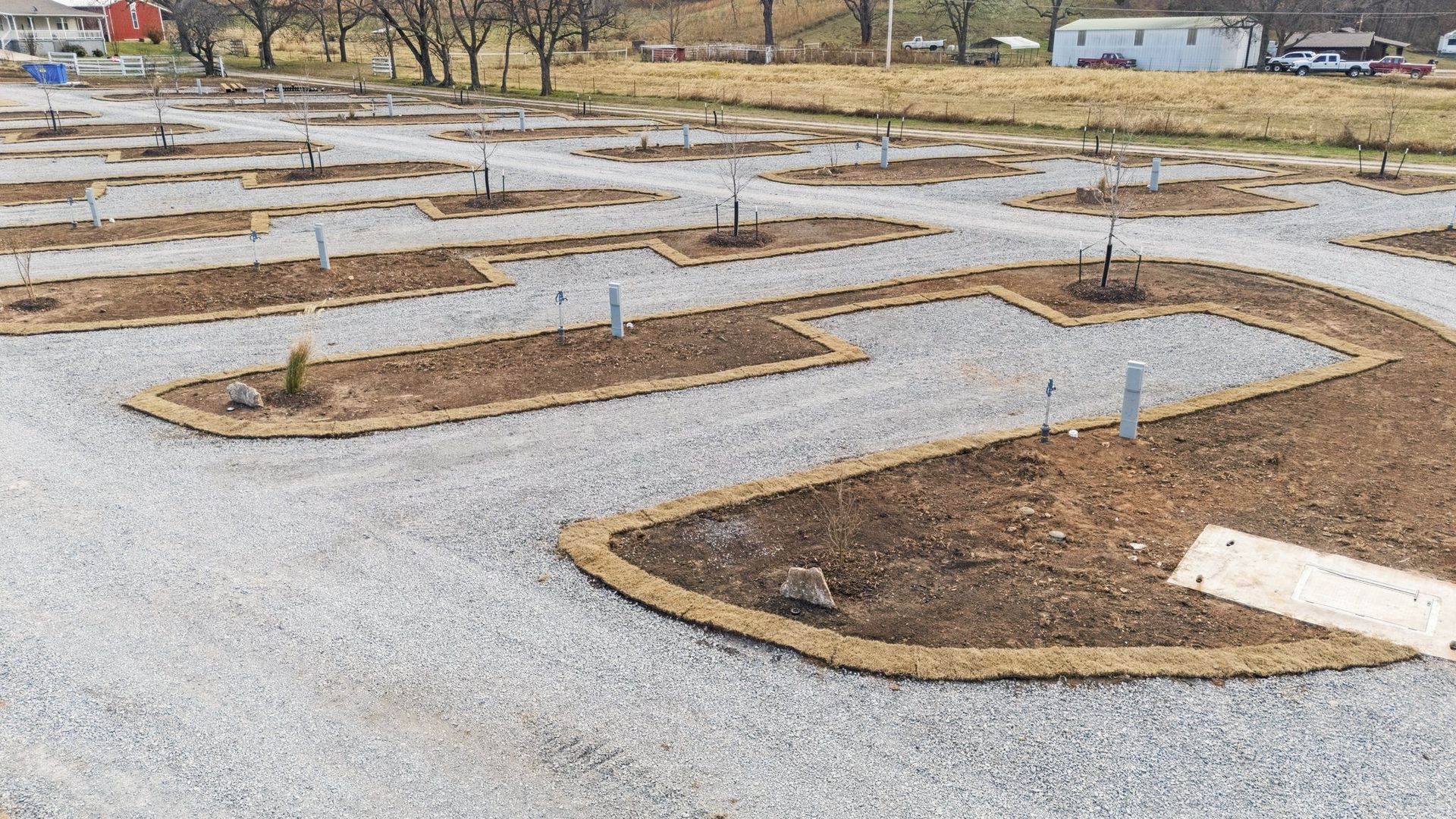 A gravel parking area with landscaped, rectangular planting beds bordered by brown edging in a clear, open lot.