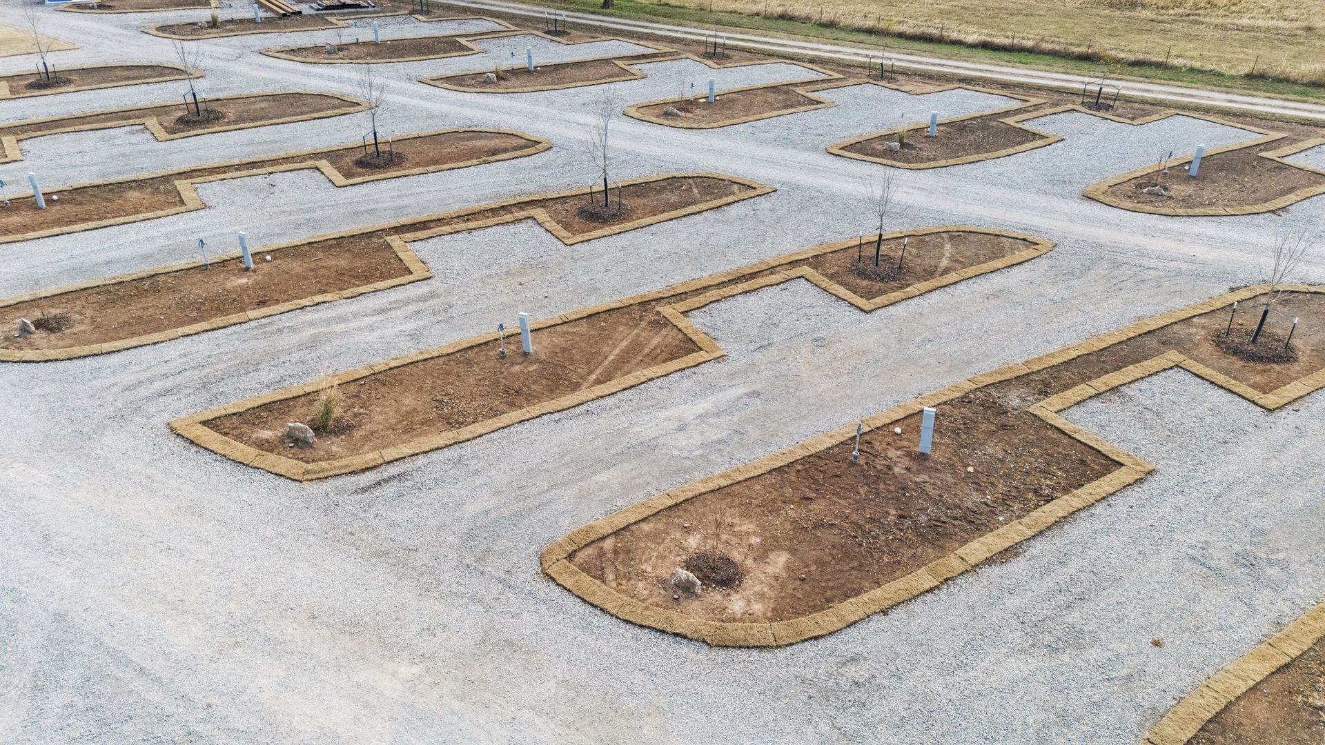 An aerial view of a grave site featuring rows of dirt plots outlined in hay, set within a gravel-covered cemetery.