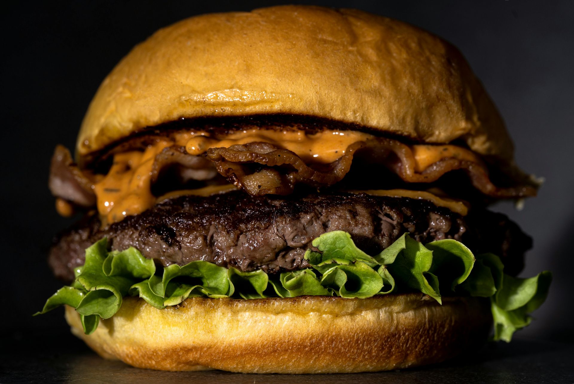 A cheeseburger with lettuce, bacon, and sauce, centered against a dark background.