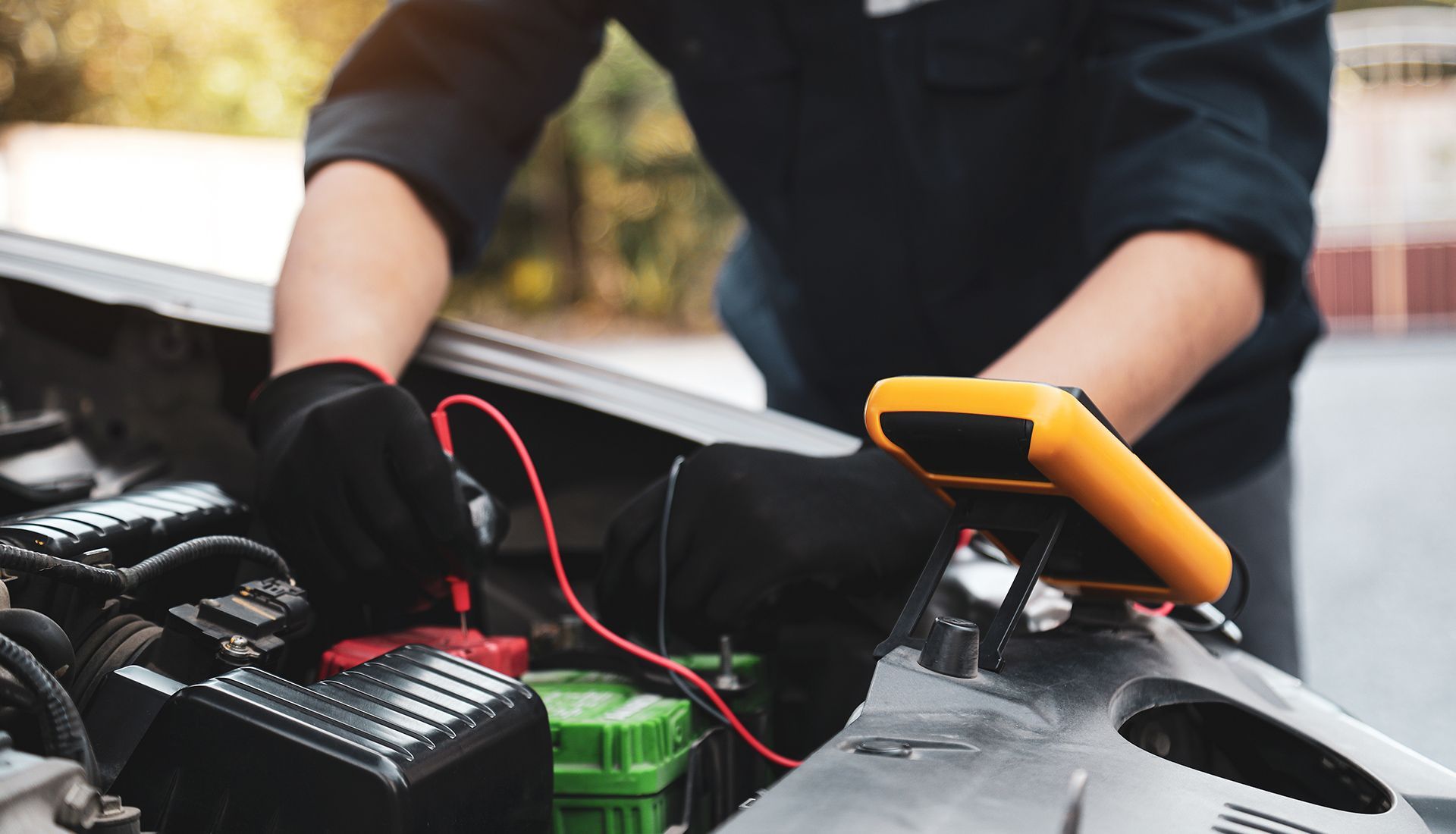 Mechanic uses a multimeter to test a car battery in an open engine bay.