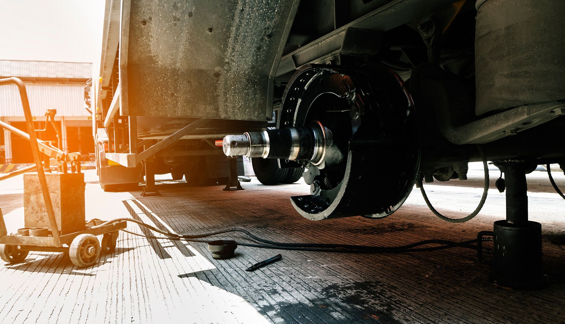 A truck tire being repaired. The hub and brake drum are exposed, with tools and a jack in the background.