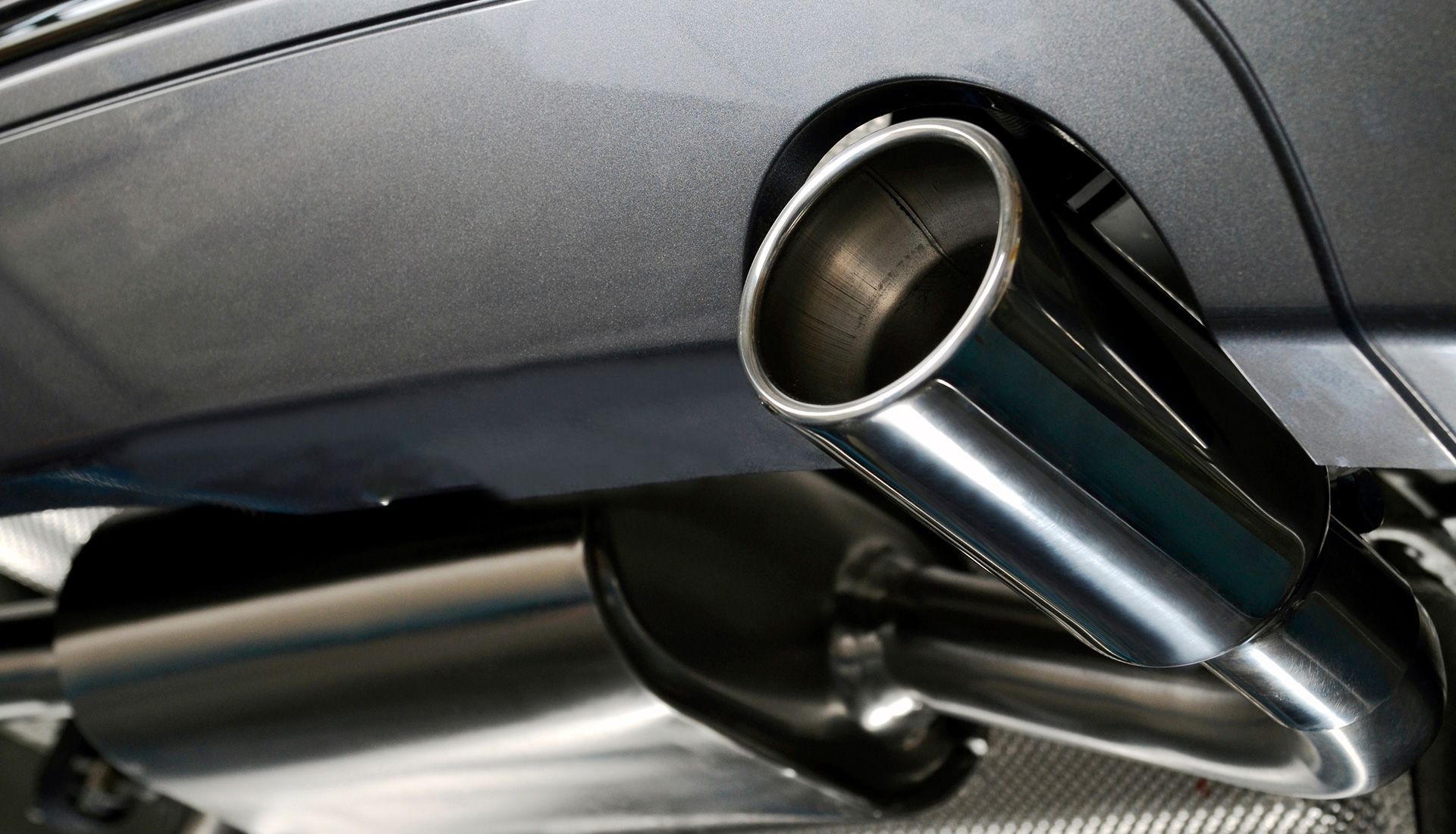 Chrome exhaust pipe and muffler under a gray car.