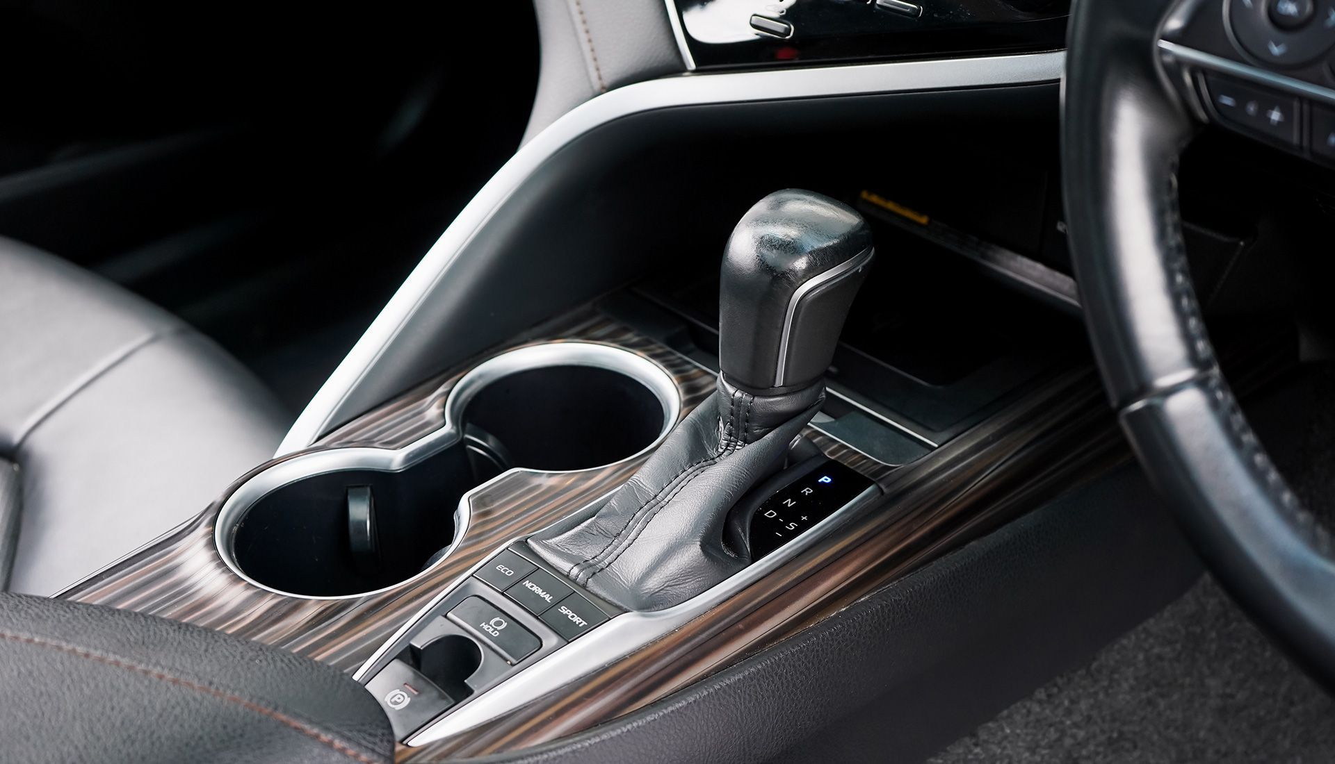 Car's interior: center console with gear shift, cup holders, and buttons on wood grain panel.