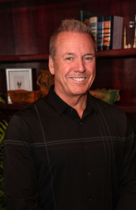 A man in a black shirt is smiling in front of a bookshelf