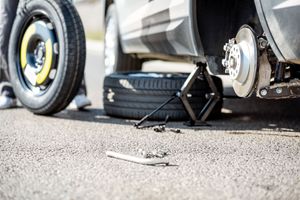 Car jack and loose wheel beside a car with a flat tire on the roadside