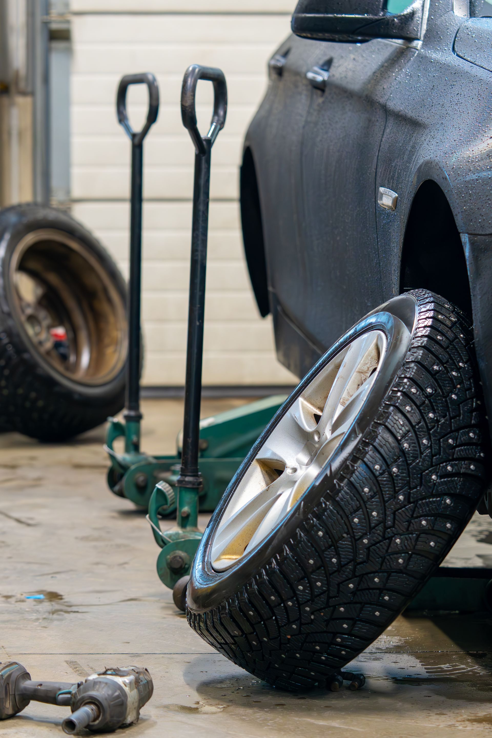 Car tire mounted on a car in a garage with tools and a spare wheel nearby