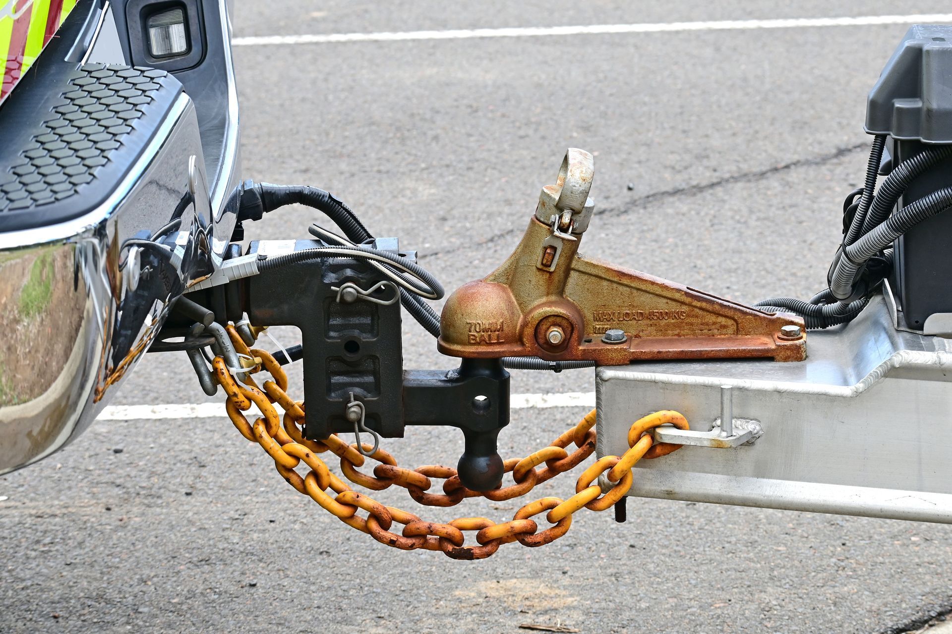 Close-up of a trailer hitch with a rusty orange safety chain connected to a silver vehicle bumper.