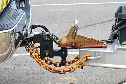 Close-up of a trailer hitch with a rusty orange safety chain connected to a silver vehicle bumper.
