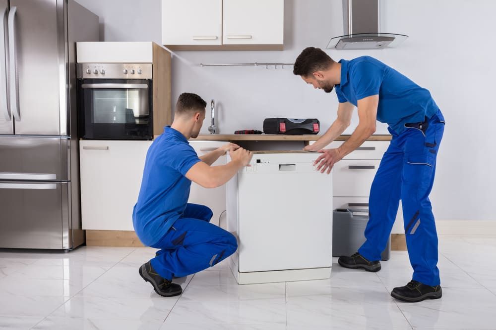 Two Men Are Working On A Dishwasher In A Kitchen — Byron Coast Removals In Mullumbimby, NSW