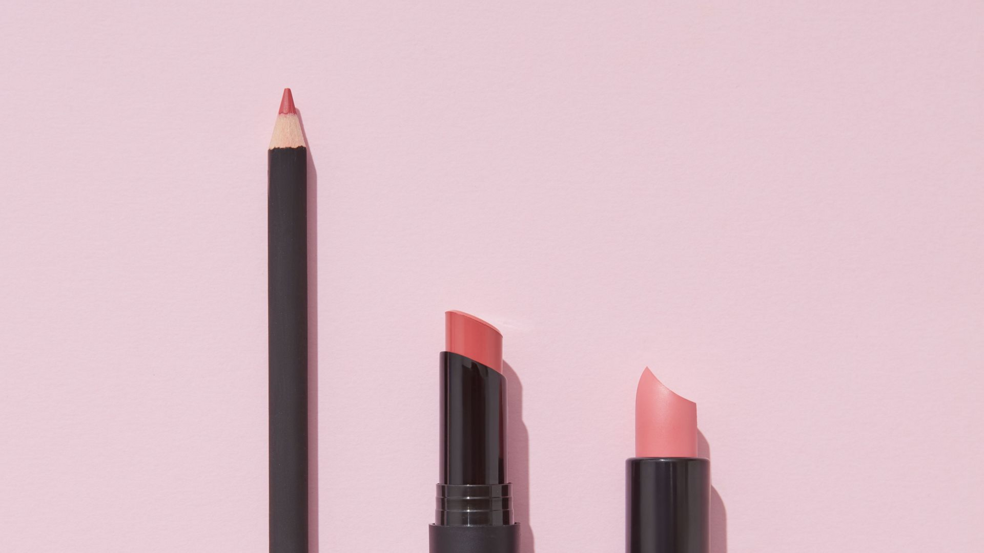 Makeup products including lipsticks and a lip pencil on a pink background