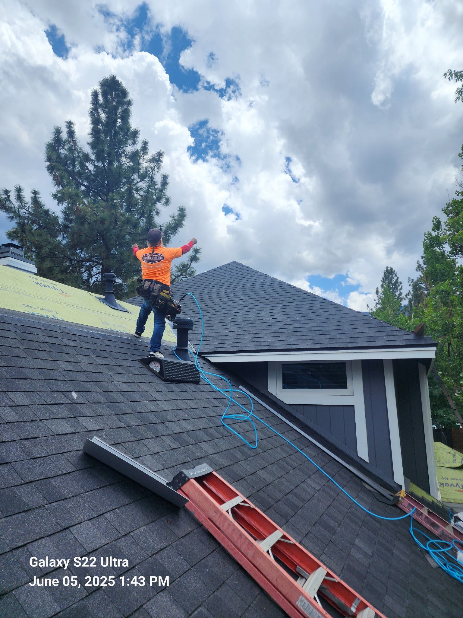 A man is standing on top of a roof next to a ladder.