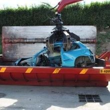 Una gru sta caricando un'auto blu in un cassonetto.