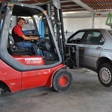 Un uomo guida un carrello elevatore accanto a un'auto in un garage.
