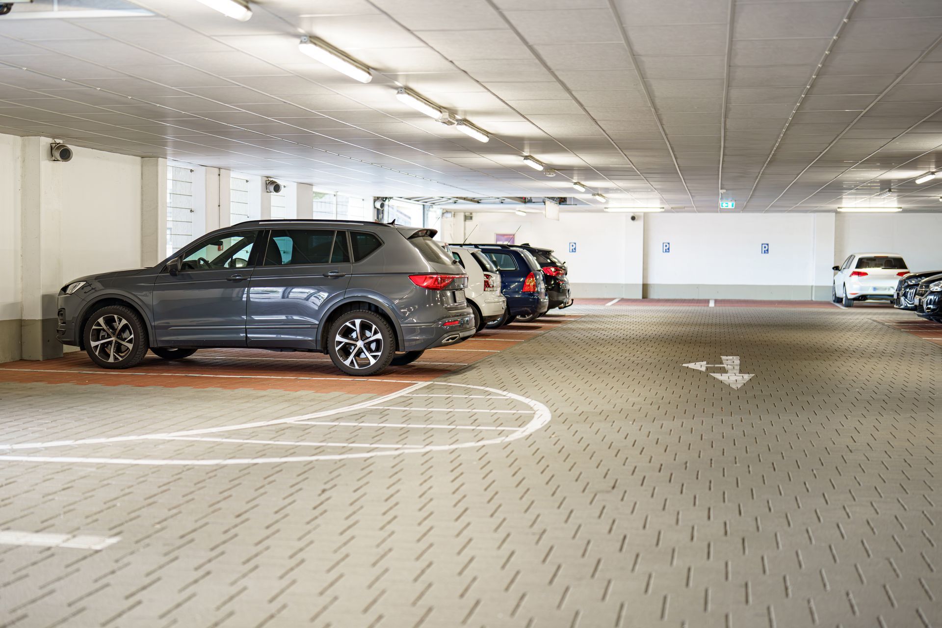 Indoor parking garage with several parked cars and directional arrows on the floor