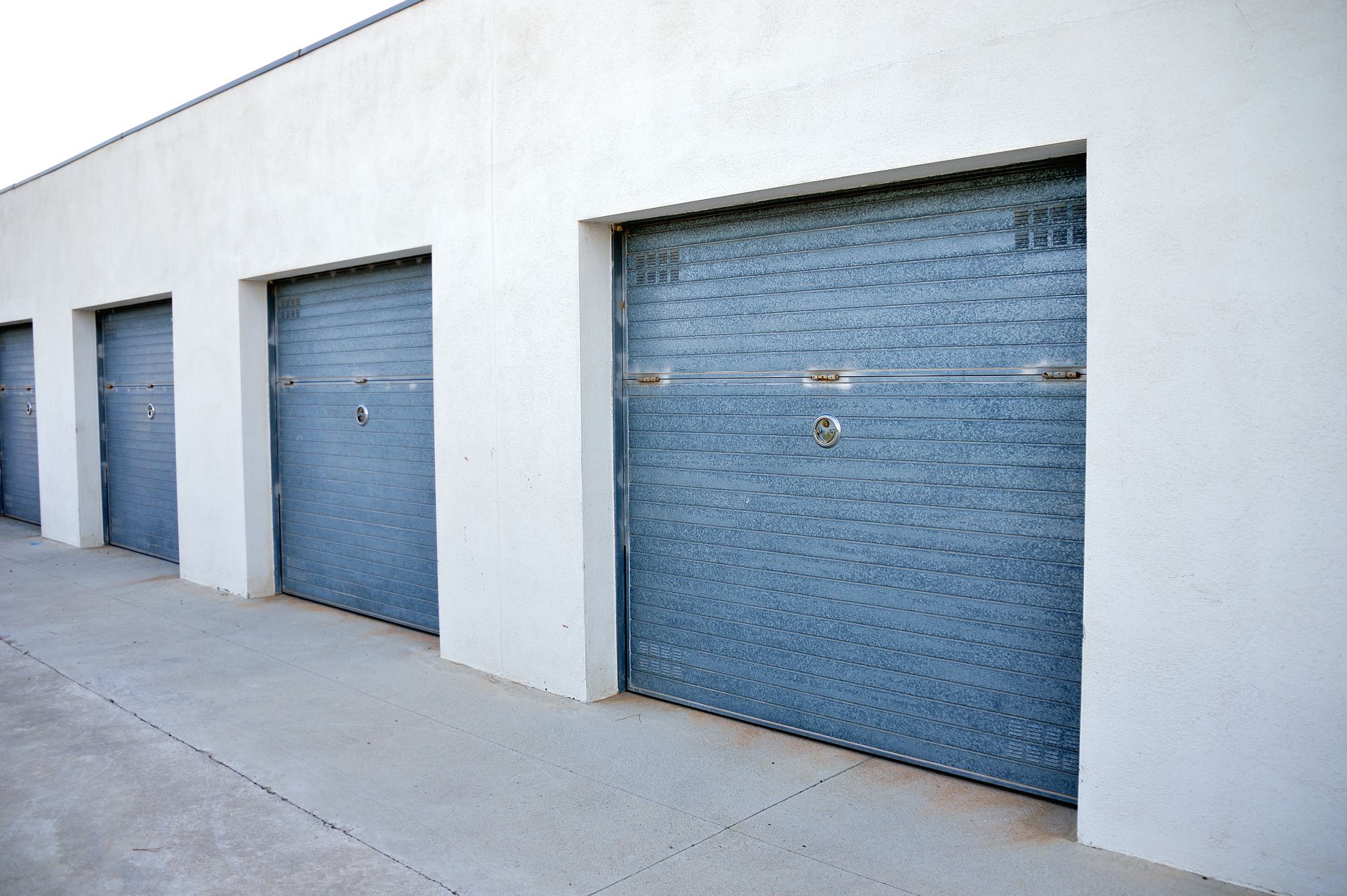 Row of closed blue garage doors on a white building exterior